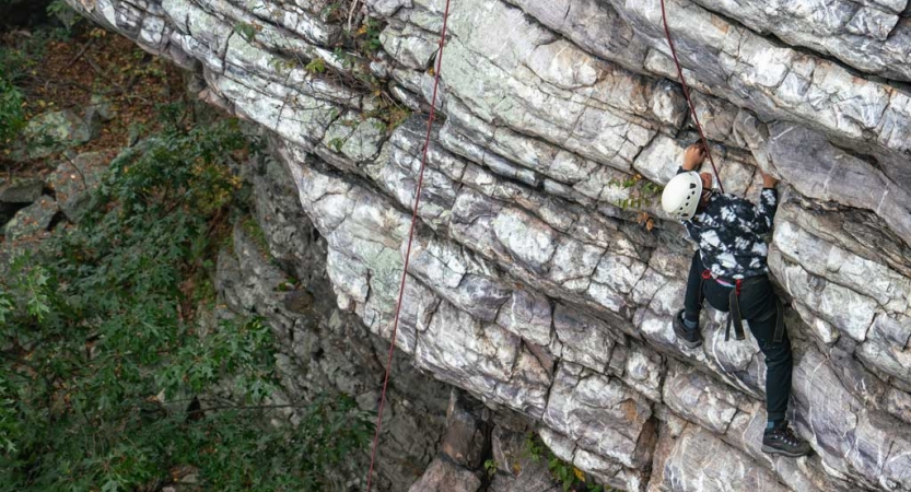 a teen scales a rock wall on a rock climbing trip with outward bound